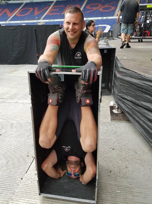 Zwei Männer stehen bei einer Box auf der Bühne, der eine ist kopfüber in der Box.