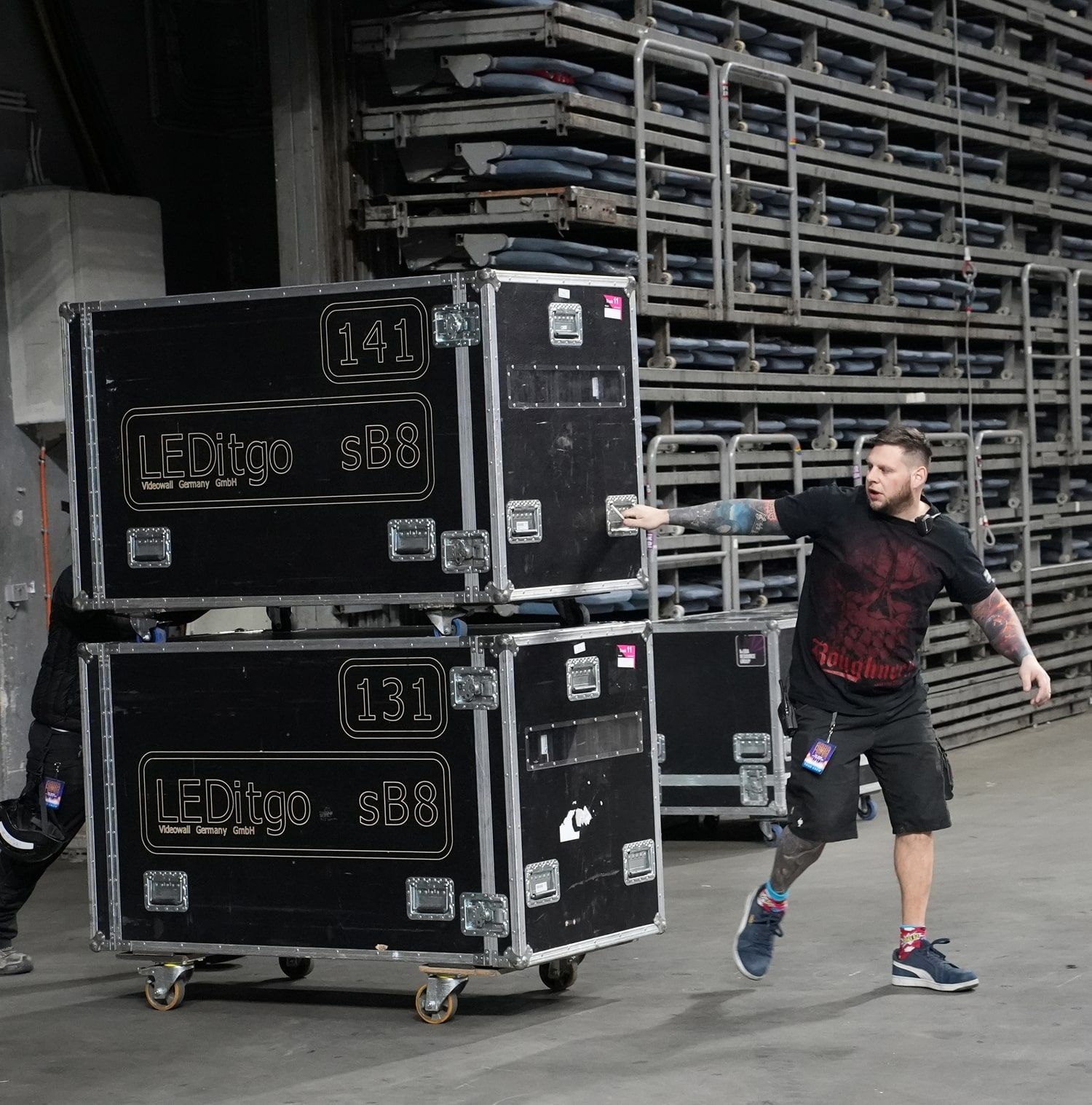 Dunkel gekleideter Mitarbeiter, welcher große Kisten mit Bühnenmaterial hinter sich her zieht.